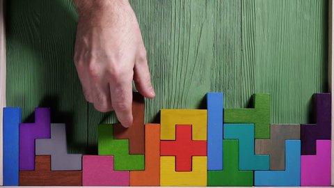 Top view on man's hand playing with colorful wooden blocks on the green wooden table background. The concept of logical thinking.