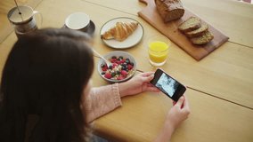 Woman sliding sea pictures on smartphone at breakfast table