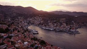 Aerial drone video of iconic port of Symi island or Yalos at sunset with beautiful scattered clouds, Symi island, Dodecanese, Greece