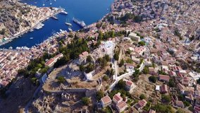 Aerial bird's eye view video taken by drone of iconic castle of Symi in Ano chora with views to port of Symi island, Dodecanese, Greece