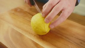 Man's Hands Cutting Whole Lemon With Knife On Chopping Board