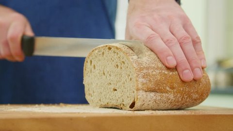 Man Slicing Crusty Loaf Of Bread With Knife In Kitchen