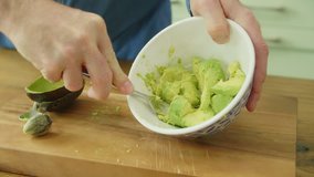 Close-up Of Man's Hands Mashing Avocado With Fork In Bowl