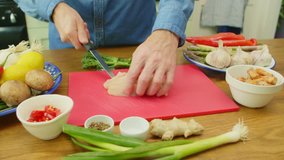 Close-up Of Man's Hands Slicing Raw Chicken On Chopping Board