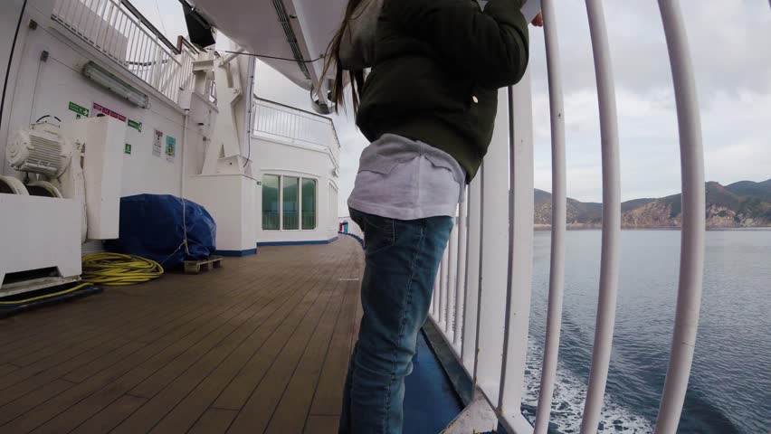A little girl travelling on a ferry boat in the sea near a green island on a cloudy weather