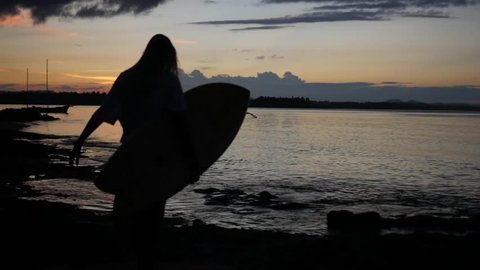 surfer Girl walking slow motion and carrying surfboard at sunset on shore