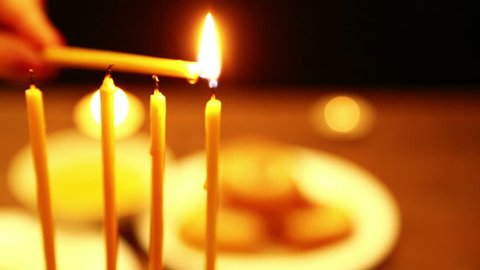 a woman holds a candle in her hand with the help of which she lights candles of Hanukkah. a woman lights candles from the first candle from right to left. close-up. the camera moves from right to left