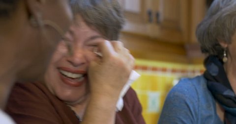 Woman wiping tears of joy with her two other friends all over 60 laughing and having a great time together at a social event