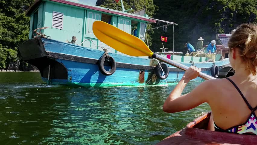 blue boat with garbage baskets and people moors at floating house near island and girl in kayak on foreground