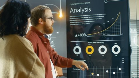 Female Developer and Male Statistician Use Interactive Whiteboard Presentation Touchscreen to Look at Charts, Graphs and Growth Statistics.  Shot on RED EPIC-W 8K Helium Cinema Camera.
