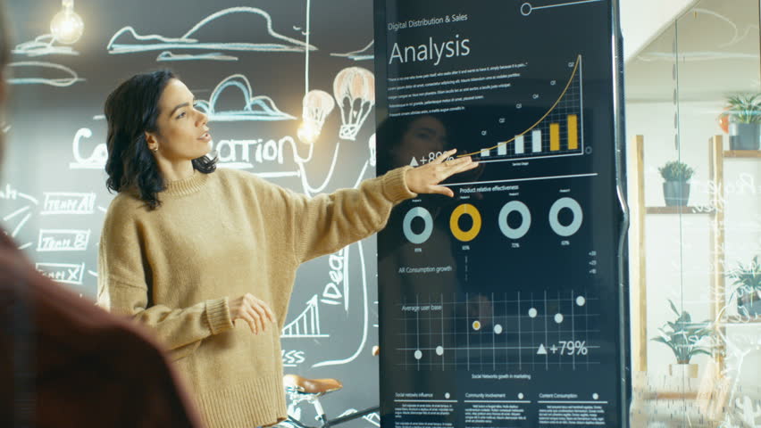 Female Project Manager Holds Meeting Shows Statistical Graphs and Charts on the Interactive Whiteboard Touchscreen Device. She Works in the Stylish Creative Agency. Shot on RED EPIC-W 8K Helium Camera
