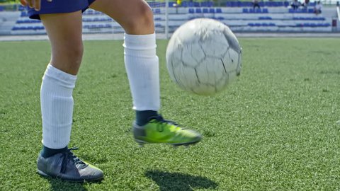 Tilt up with slow motion of blond boy from junior soccer league juggling ball on leg in outdoor playing field on sunny summer day