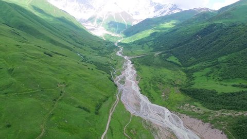 Flying over rocky mountain river in green valley 4k Aerial view nature video landscape background panorama. Water flows, snow peak green ridge hills on blue sky and clouds in Caucasus, Georgia