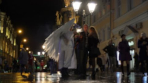 Man in costume love Angel Cupid on night city streets and lovers couples. Concept Christmas, New year, Valentine's day, carnival. Angel holds bow and lit Sparkler and makes selfie with couples in love