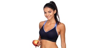 Pleased brunette fitness woman eating big apple and looking at the camera over white background
