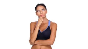 Pensive brunette fitness woman holding her chin and pointing at the camera over white background