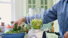 Woman Adding Kale And Water In Blender At Kitchen
