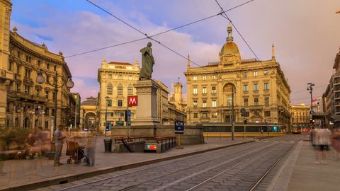 Cordusio Square and Dante street with surrounding palaces, houses and buildings at sunset timelapse in Italian capital of fashion and luxury. Monument to writer and poet Giuseppe Parini. Trams passing