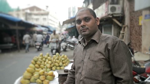 A street fruit vendor or seller in India looking into a camera and smiling