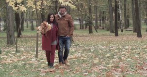 Loving couple walking with leaves bouquet in hands in autumn forest park 4k video. Young man and overweight fat woman romantic date. Love story romance concept