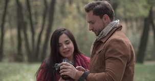 Loving couple photographing in autumn forest park 4k date video. Young man and overweight fat woman looking photo shoots on digital camera. Love story romance concept