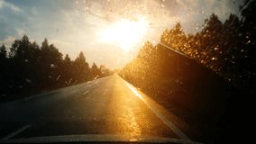 Driver's perspective. travelling along a straight highway. with windshield wipers clearing raindrops as they are illuminated by the setting sun. UHD 4k video