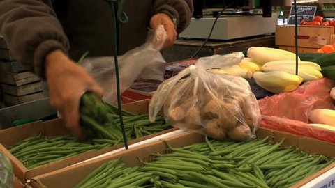 Vendor grabs handfuls of freshly grown green beans, places them in plastic bag for customer at farmer’s market. 1080p Stock Video