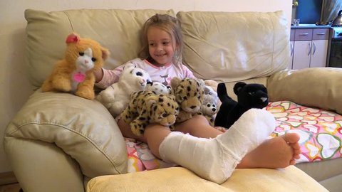 Girl with broken leg in plaster sit and play soft toys at home couch