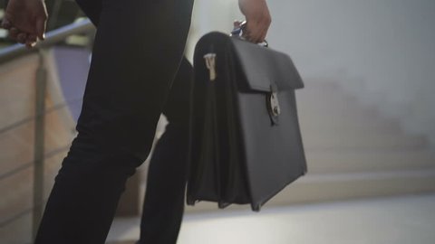 Slow motion: Unrecognizable businessman or lawyer in formal suit with briefcase goes upstairs in centrelink offices of company or in the building of state authority.