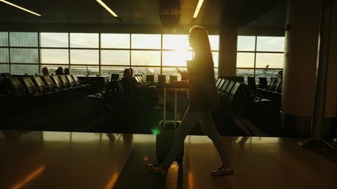 A business woman with a smartphone in her hand and a heap of luggage walks the terminal of the international airport.