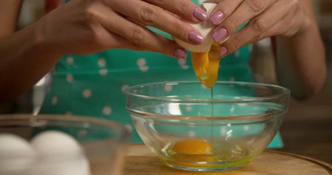 Woman hand breaking eggs into bowl slow-motion 4k close-up video. Female preparing cooking food at home kitchen. Cracking egg yolk white pouring falling.