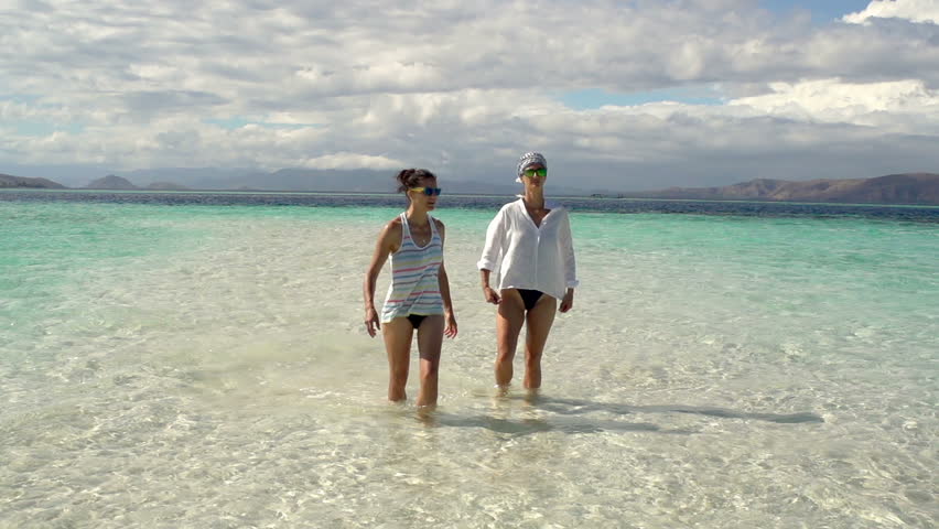 Women walking in the clear sea and waving to the camera, steadycam shot, slow motion shot at 240fps
