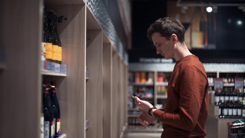 Young man chooses wine taking photo of bottles at supermarket | Shutterstock HD Video #33448291