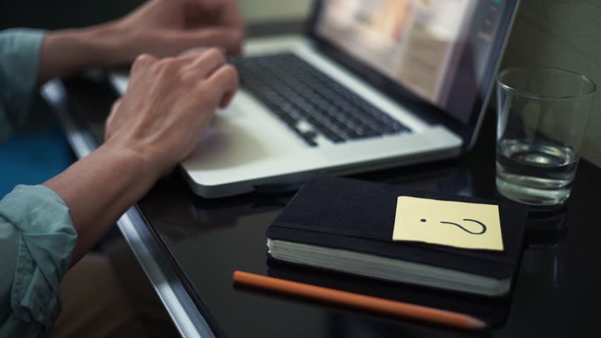 Young man scrolling laptop at home. Sticky note with question sign on desk