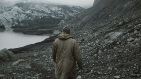 Back view of young man walking in ice lagoon alone. Traveling male hiking in volcanic mountains near glaciers in Iceland: film stockowy