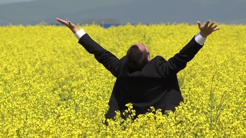 Happy man with suit raising up hands in rape field, enjoy richness of business