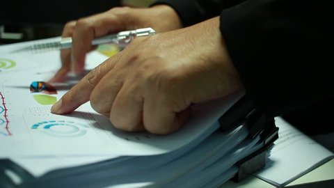 Businessman Preparing reports papers with graphs, charts on Stacks of documents files for finance in office. Piles of unfinished document achieves with paper clip. Concept of Business Annual Report.