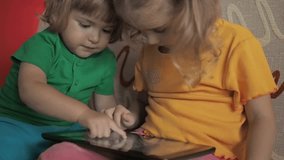 Pretty little girl, boy  sitting on sofa using laptop. An adorable children sit together and play with a laptop and digital tablet. 
