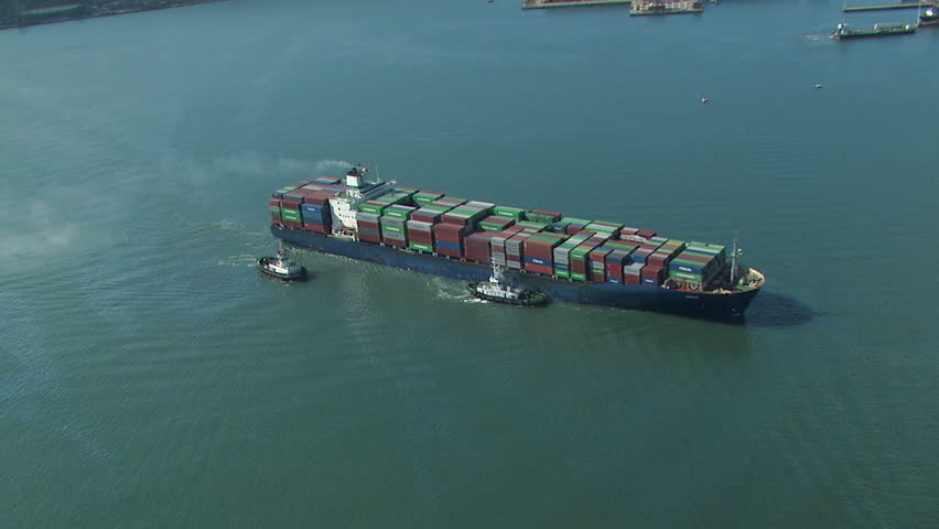 Aerial of cargo ship being assisted by tug boats and fully loaded with