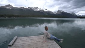 Young man sitting on wooden lake pier looking at spectacular mountain scenery in Jasper national park, Canada
People travel relaxation nature concept
