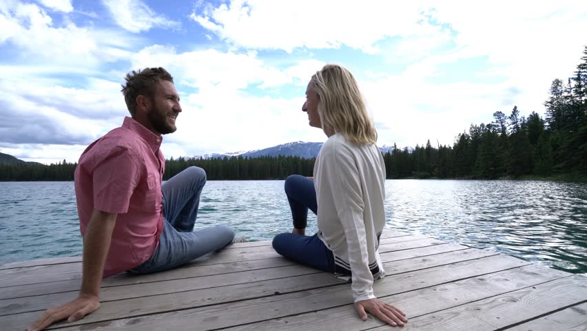 Cheerful young couple on lake pier making a heart shape finger frame on  beautiful landscape. People love nature concept. Shot in Jasper national park, Canada