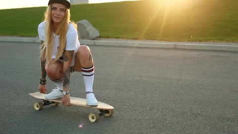 sport, lifestyle, Extreme and people concept - Beautiful girl tattoos riding longboard on the road in the city in sunny weather. Portrait hipster girl smiling with a longboard at sunset. Slow motion