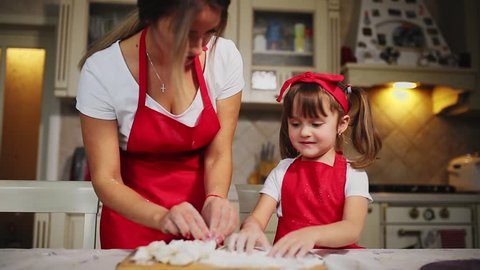 Happy family in the kitchen mom and daughter in the kitchen playing with flour to have fun and mold the patties in the kitchen in the same red aprons. stedicam