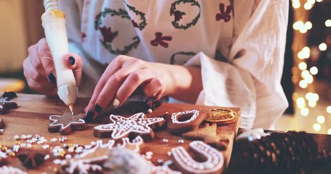 Woman Decorating Baked Gingerbread Christmas Cookies. 4K SLOW MOTION.  Female hands frosting and icing fresh holiday bakery. Festive food, family, Christmas and New Year traditions concept., videoclip de stoc
