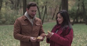 Loving couple speaking with leaves in hands in autumn forest park 4k video. Young man and girl laughing romantic date. Love story romance concept
