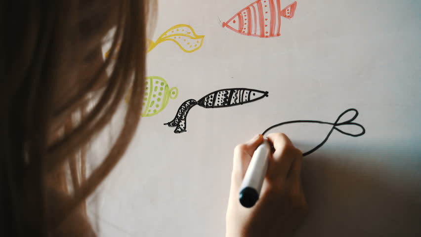 Child girl drawing fishes with the marker on a whiteboard
