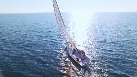 Aerial footage from drone, of professional speed yacht or sailboat leaning to one side, ready to make a maneuvre, wind in mainsail attached to mast, team race or competition, with sun flares