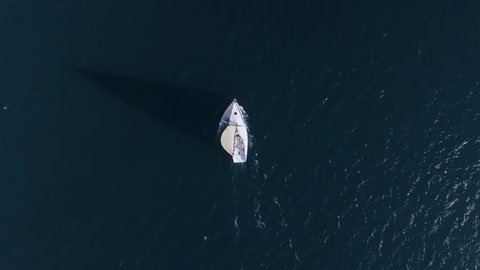 Top view from aerial drone from high in sky of small white sailboat during adventures or exploring of new land, moves on high nautical speed through blue waters of sea or ocean 库存视频