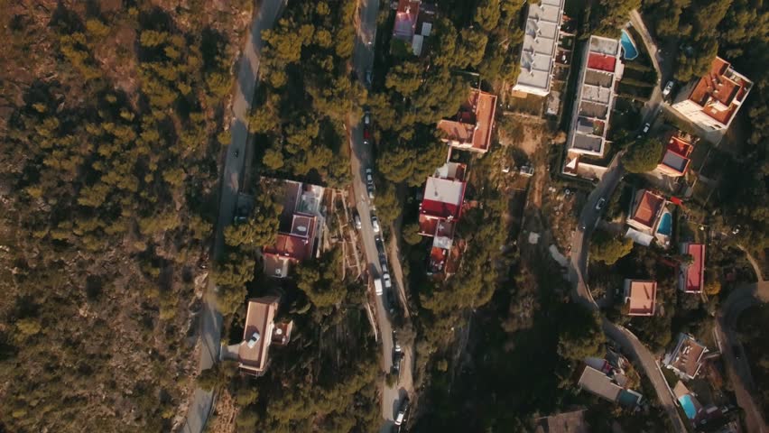 Aerial footage above curved mountain roads with tiny houses next to forest. Small cars and motorcycle ride on it
