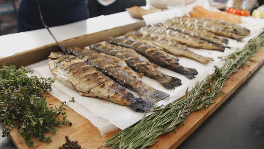 Grilled fish with rosemary. A lot cooked fish with greens on the table at the food festival. Delicious salmon cooked on barbecue.